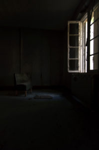 Une pièce abandonnée et plongée dans la pénombre : une fenêtre éclaire simplement un fauteuil vide